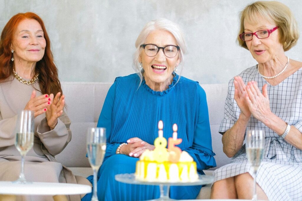 Three older friends celebrating a birthday with sparkling drinks and a birthday cake in an Oakville retirement residence community.